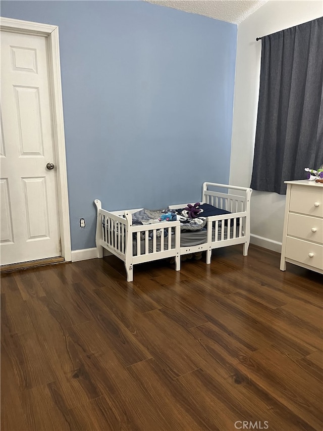 bedroom featuring dark wood-style floors, a crib, baseboards, and a textured ceiling