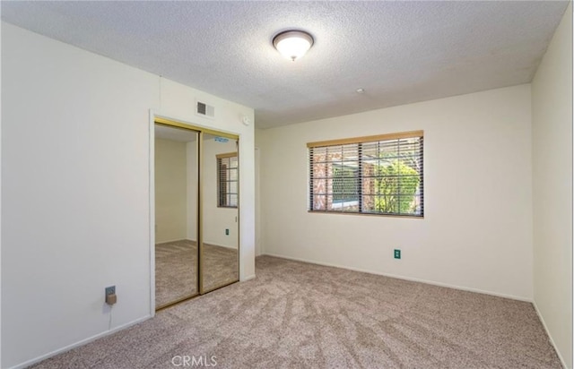 unfurnished bedroom featuring light colored carpet, a closet, and a textured ceiling