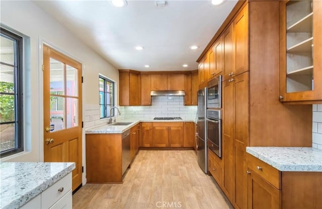 kitchen with appliances with stainless steel finishes, sink, backsplash, light stone countertops, and light wood-type flooring