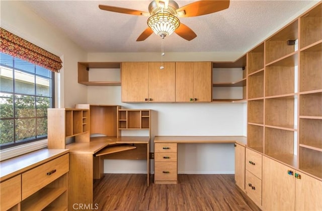 unfurnished office with ceiling fan, built in desk, dark hardwood / wood-style floors, and a textured ceiling