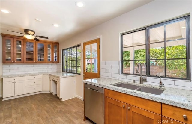 kitchen with sink, light wood-type flooring, stainless steel dishwasher, light stone countertops, and backsplash