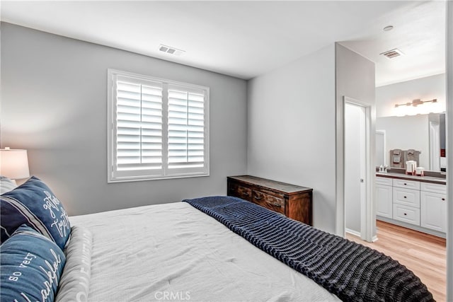 bedroom with ensuite bathroom, sink, and light hardwood / wood-style flooring