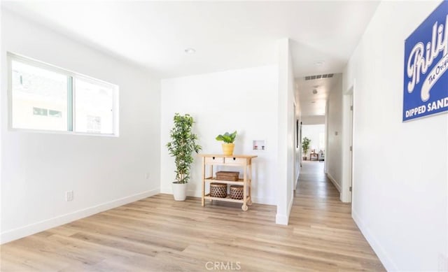 hall featuring baseboards, visible vents, and light wood-style floors