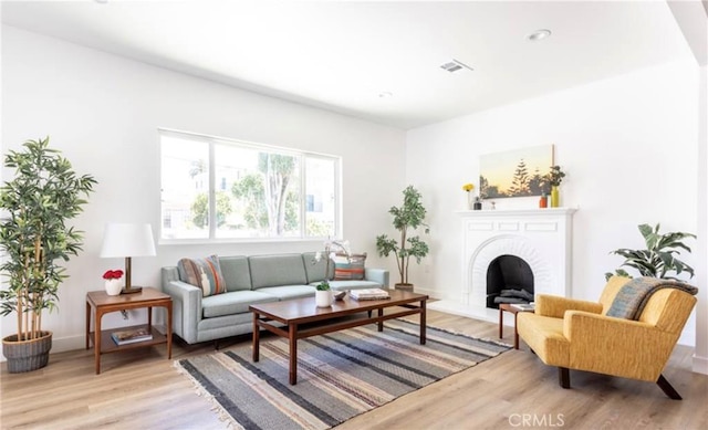 living area with a fireplace with raised hearth, visible vents, light wood-style flooring, and baseboards