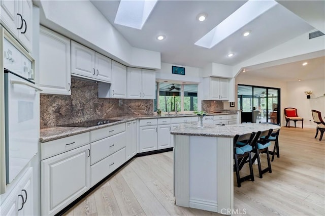 kitchen with light stone countertops, a kitchen island, black electric stovetop, and white cabinets