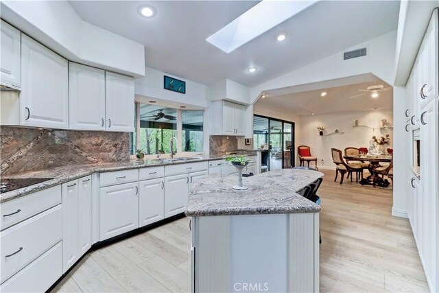 kitchen featuring sink, vaulted ceiling with skylight, white cabinets, and light stone counters