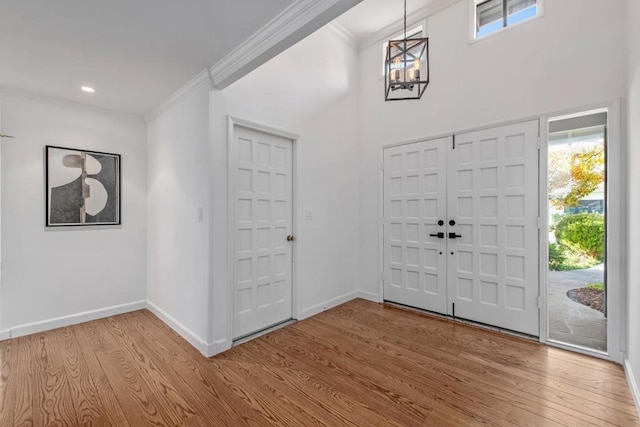 foyer featuring crown molding, a chandelier, a high ceiling, and light hardwood / wood-style floors