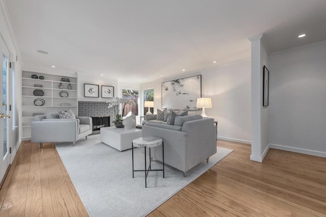 living room featuring crown molding, built in features, light hardwood / wood-style floors, and a brick fireplace