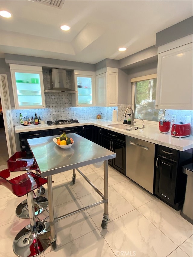 kitchen featuring tasteful backsplash, appliances with stainless steel finishes, white cabinetry, wall chimney exhaust hood, and sink