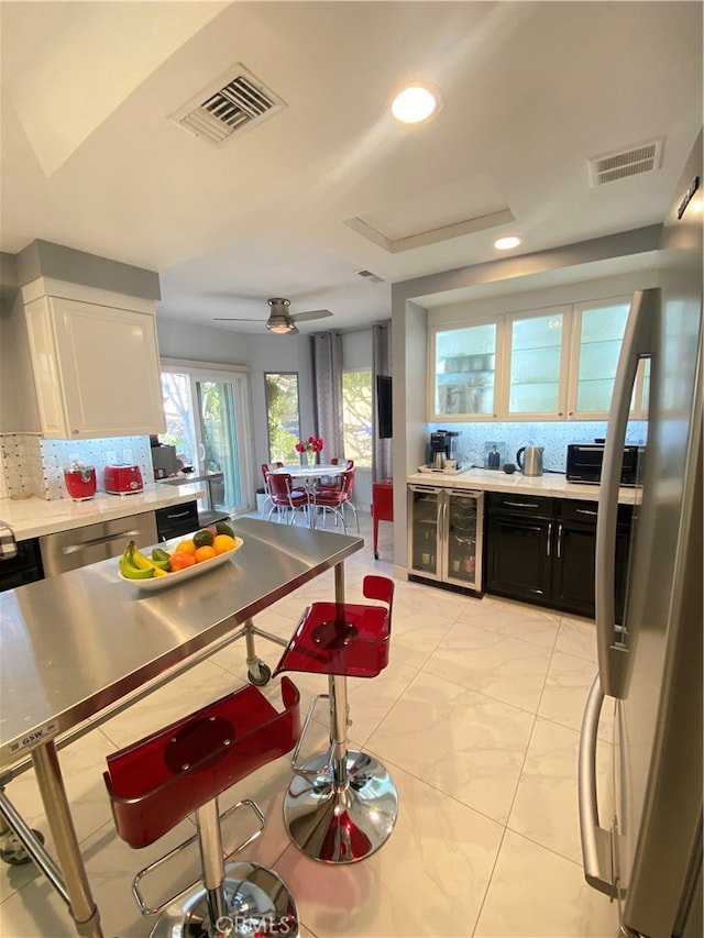 kitchen with white cabinetry, stainless steel fridge with ice dispenser, backsplash, and ceiling fan