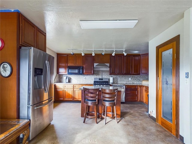 kitchen featuring a breakfast bar, rail lighting, tasteful backsplash, range hood, and appliances with stainless steel finishes