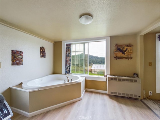 bathroom with a washtub, a textured ceiling, hardwood / wood-style flooring, and radiator