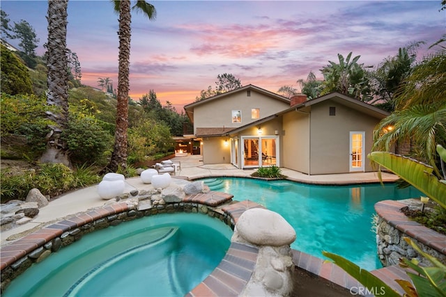 pool at dusk with a patio and an in ground hot tub