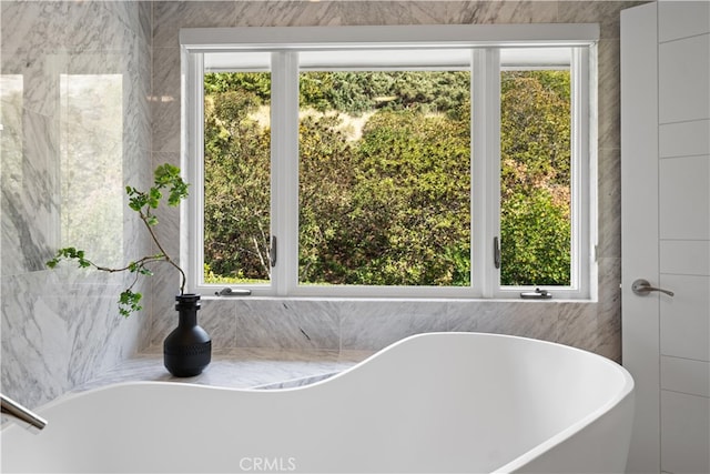 bathroom featuring a tub to relax in, tile walls, and a healthy amount of sunlight