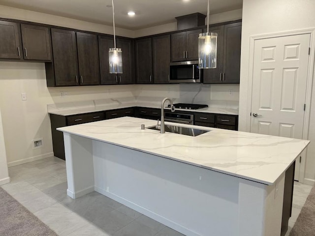 kitchen with hanging light fixtures, an island with sink, sink, and light stone counters