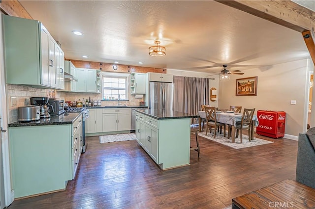 kitchen featuring appliances with stainless steel finishes, dark hardwood / wood-style flooring, a kitchen breakfast bar, ceiling fan, and a kitchen island