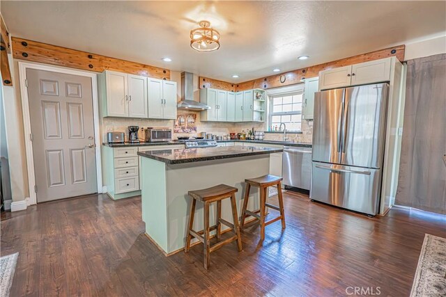 kitchen with appliances with stainless steel finishes, wall chimney exhaust hood, dark wood-type flooring, white cabinets, and a kitchen island