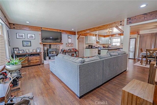 living room featuring beam ceiling, wood-type flooring, and a wood stove