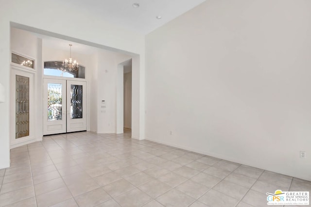 spare room featuring a notable chandelier, french doors, light tile patterned flooring, and lofted ceiling