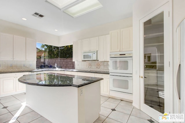 kitchen with decorative backsplash, dark stone counters, a center island, white cabinetry, and white appliances