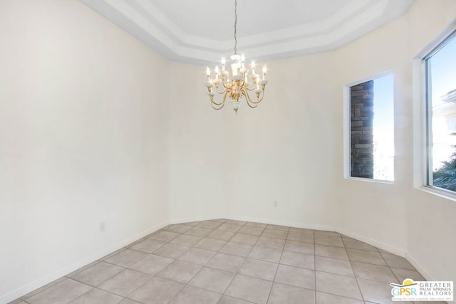 spare room with light tile patterned floors, a chandelier, a tray ceiling, and a wealth of natural light