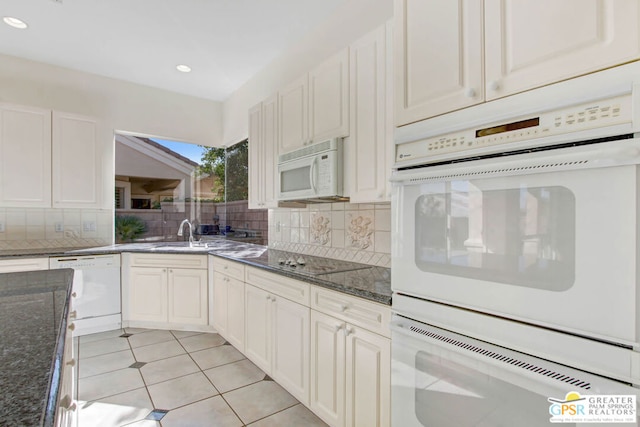 kitchen with dark stone counters, sink, light tile patterned flooring, white appliances, and tasteful backsplash