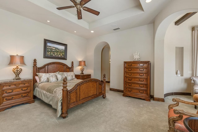 bedroom with a raised ceiling, light colored carpet, and ceiling fan