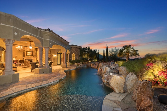 pool at dusk featuring pool water feature and a patio