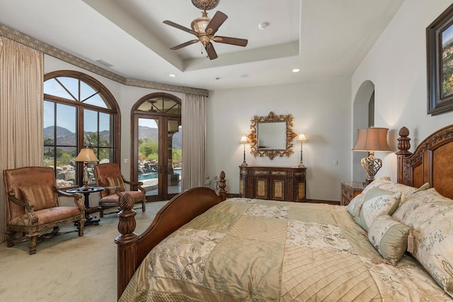 carpeted bedroom featuring access to exterior, a mountain view, a tray ceiling, and ceiling fan