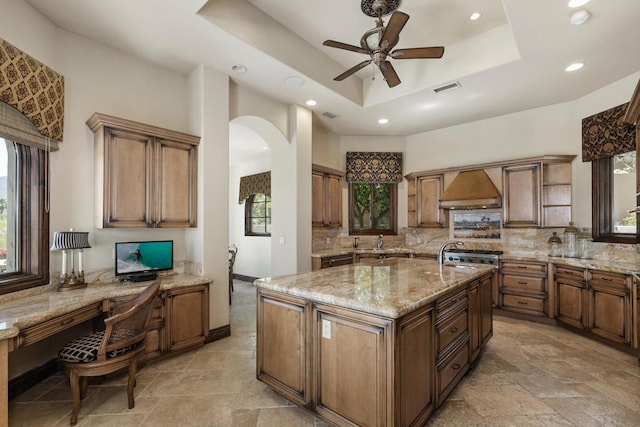 kitchen featuring a wealth of natural light, a center island with sink, a raised ceiling, and ceiling fan