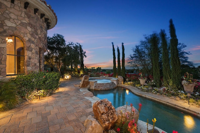 pool at dusk featuring an in ground hot tub and a patio