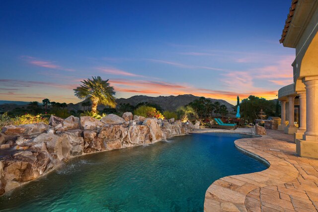 pool at dusk featuring pool water feature, a mountain view, and a patio area