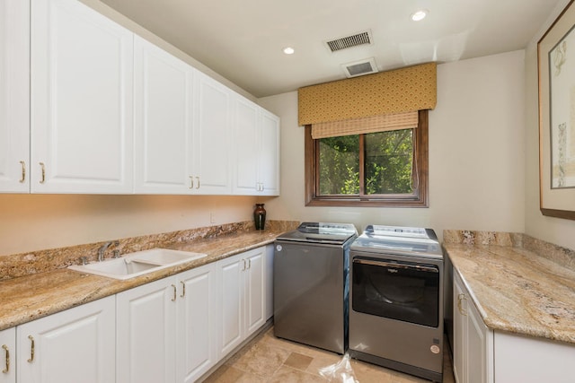 clothes washing area featuring sink, washer and clothes dryer, and cabinets