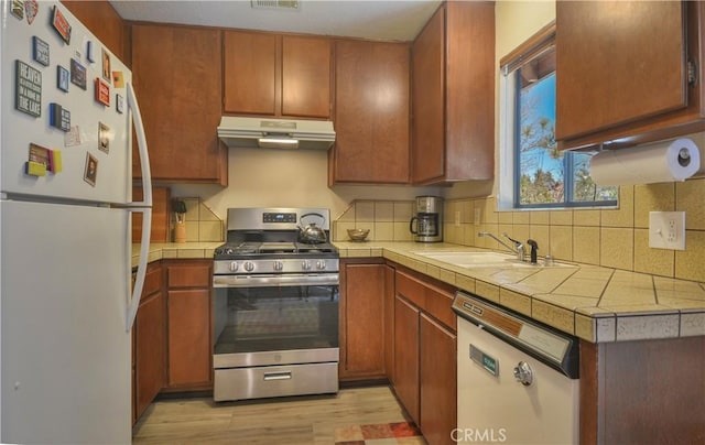 kitchen with sink, white appliances, light hardwood / wood-style flooring, tasteful backsplash, and tile countertops