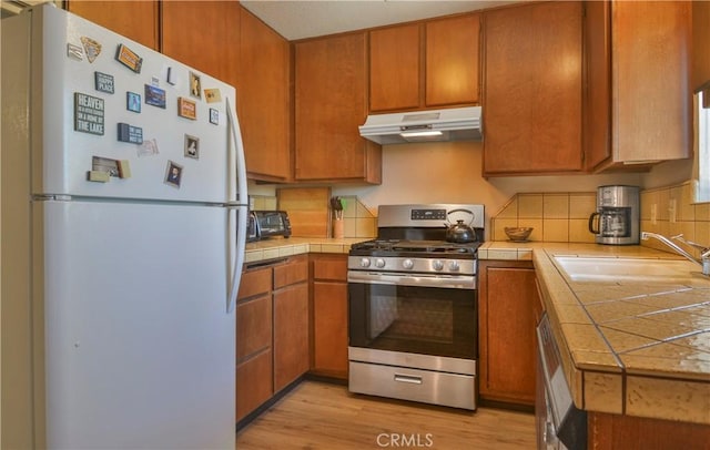 kitchen with stainless steel gas range, sink, tile countertops, light hardwood / wood-style flooring, and white refrigerator