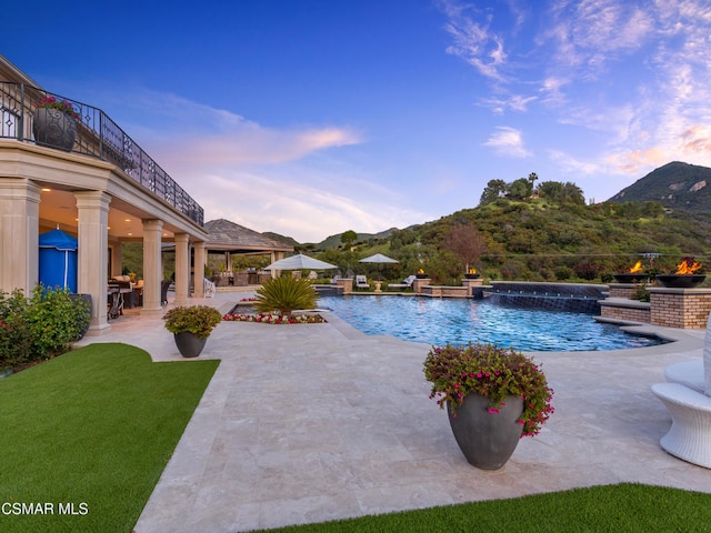 pool at dusk featuring a yard, a mountain view, and a patio