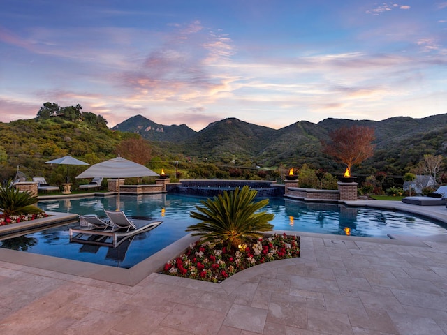 pool at dusk featuring a patio, a mountain view, and a jacuzzi