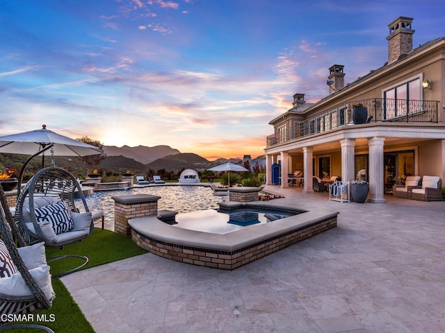 patio terrace at dusk with a balcony, an in ground hot tub, an outdoor living space, and a mountain view