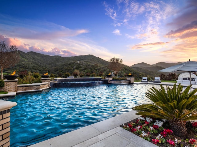 pool at dusk with an in ground hot tub and a mountain view