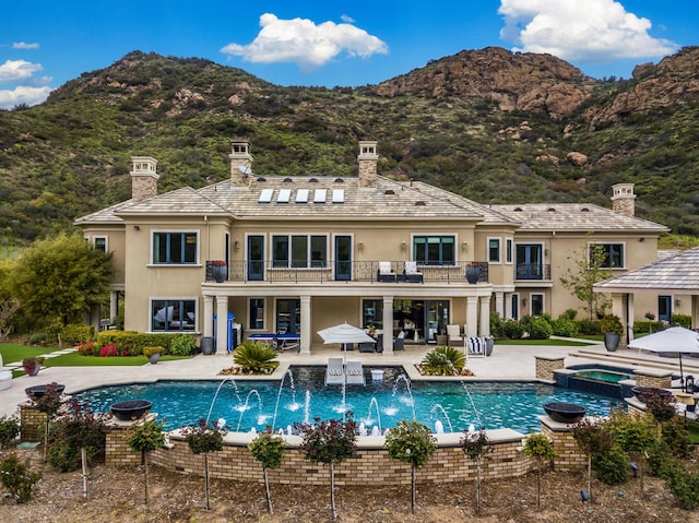 back of house featuring pool water feature, a patio, a swimming pool with hot tub, a mountain view, and a balcony