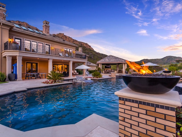 pool at dusk with a patio, a mountain view, an outdoor fire pit, and a gazebo