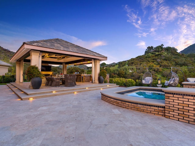 pool at dusk with a gazebo, a mountain view, a patio, and a jacuzzi