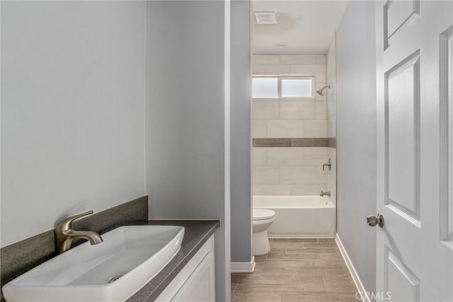 full bathroom with vanity, wood-type flooring, tiled shower / bath combo, and toilet