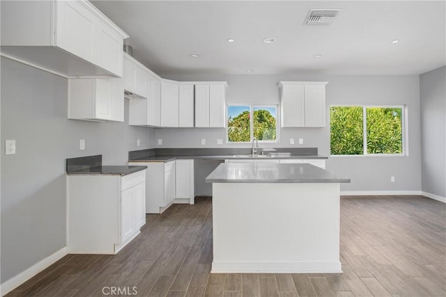 kitchen with white cabinets, plenty of natural light, a center island, and wood-type flooring