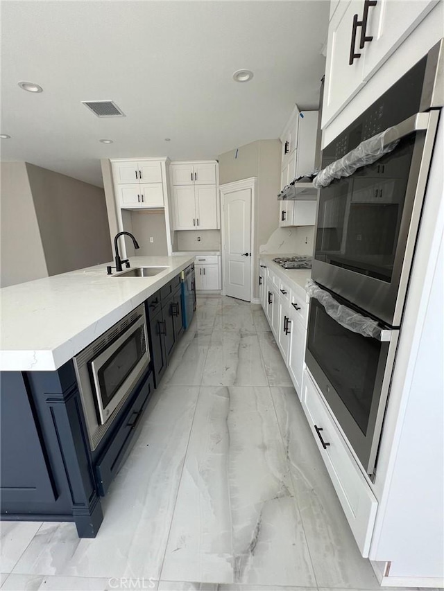 kitchen with a large island with sink, sink, white cabinetry, stainless steel appliances, and blue cabinets