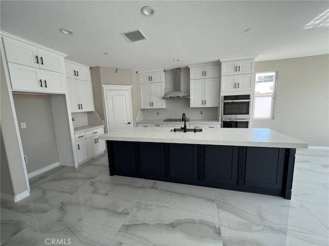 kitchen featuring white cabinetry, appliances with stainless steel finishes, wall chimney range hood, a large island with sink, and sink