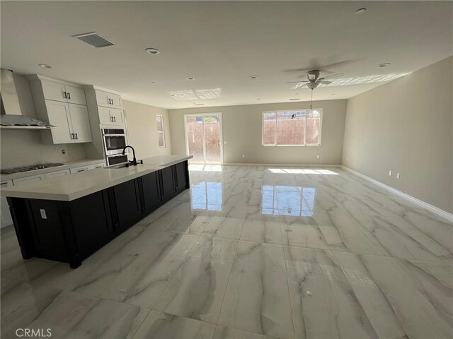 kitchen featuring white cabinets, sink, wall chimney exhaust hood, and an island with sink