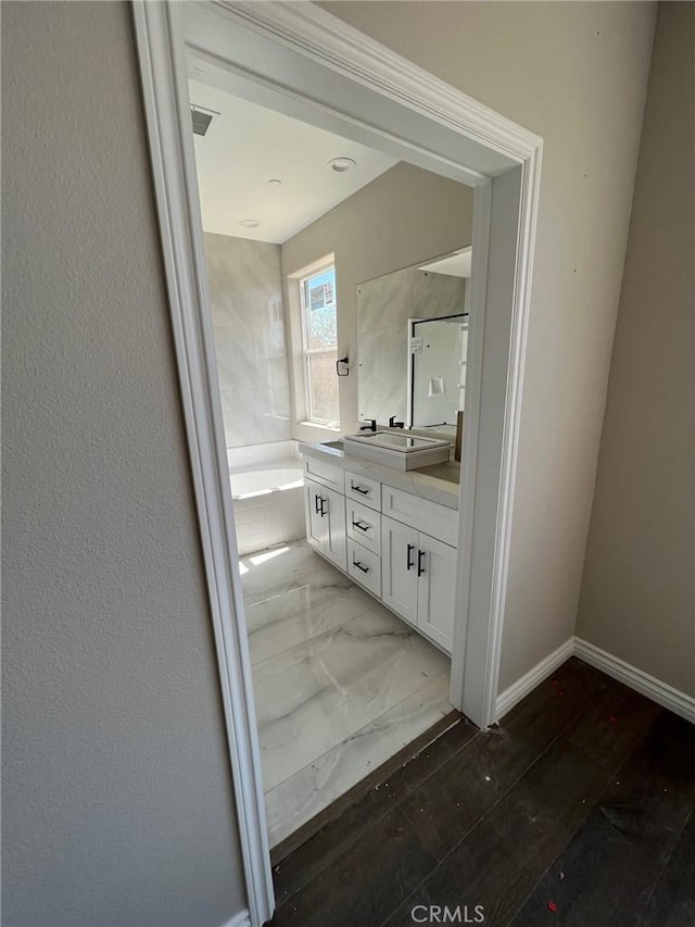 bathroom featuring a relaxing tiled tub and vanity