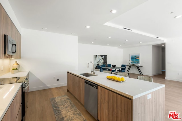 kitchen with appliances with stainless steel finishes, light hardwood / wood-style flooring, a large island, and sink