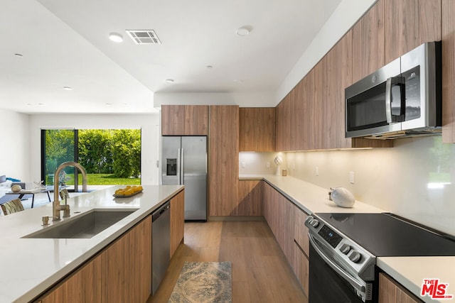 kitchen with stainless steel appliances, backsplash, sink, and light hardwood / wood-style floors